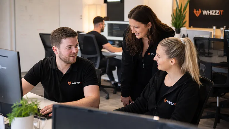 WhizzIT team members in branded tops reviewing IT support work together at a desk